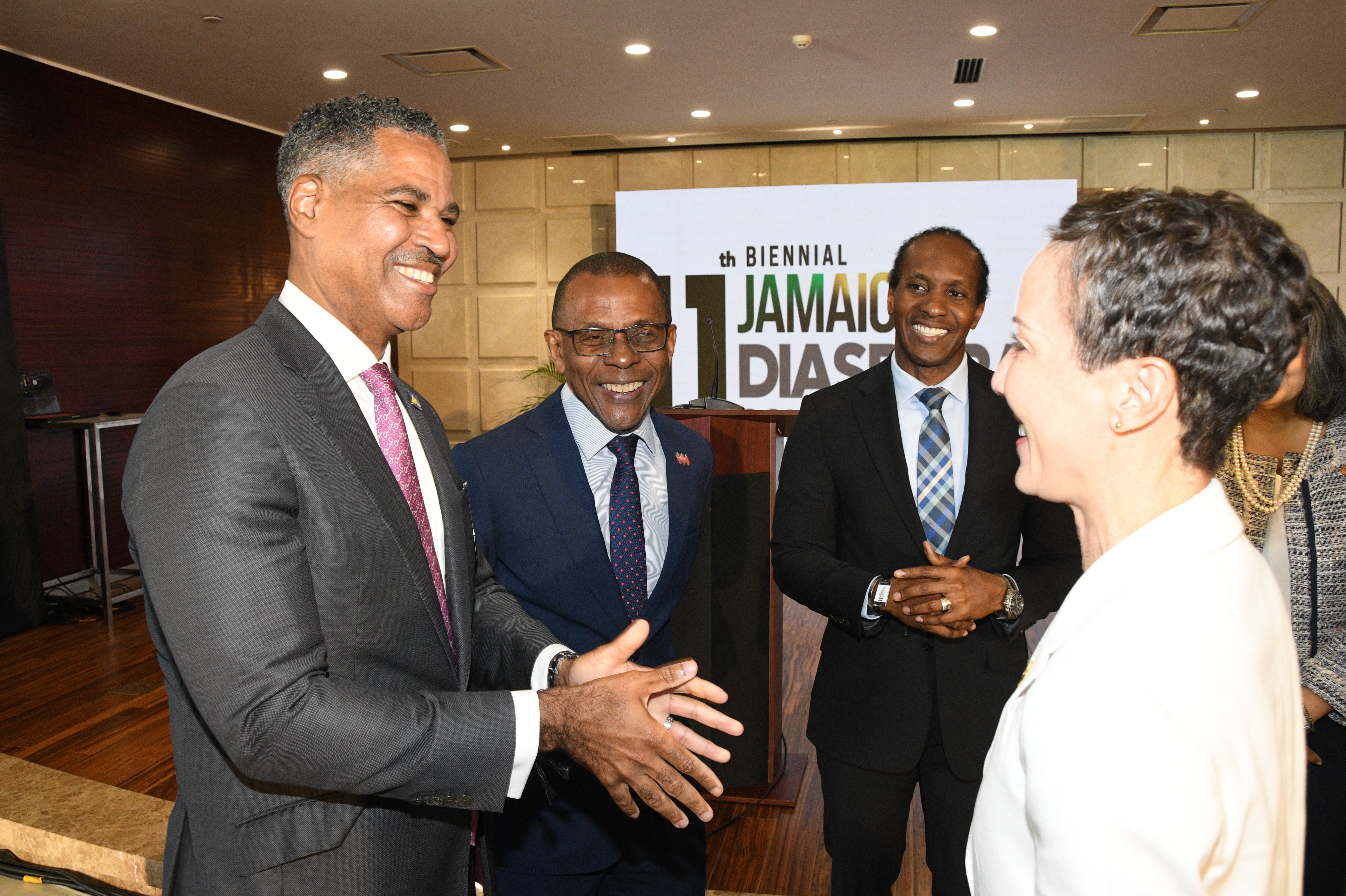 Group of professionally dressed people smiling and talking at a conference, with a Jamaica Diabetes banner in the background.