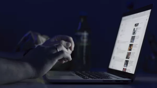 Person typing on a laptop at night, with a social media feed visible on the screen.