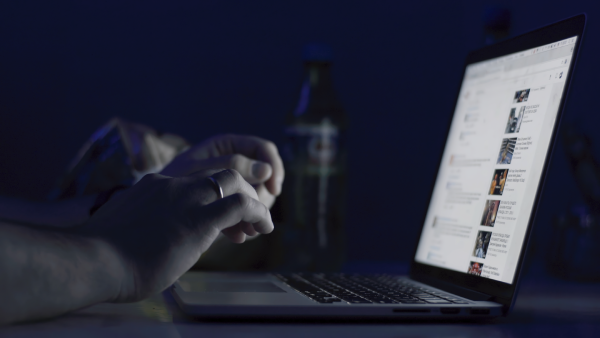 Person typing on a laptop at night, with a social media feed visible on the screen.