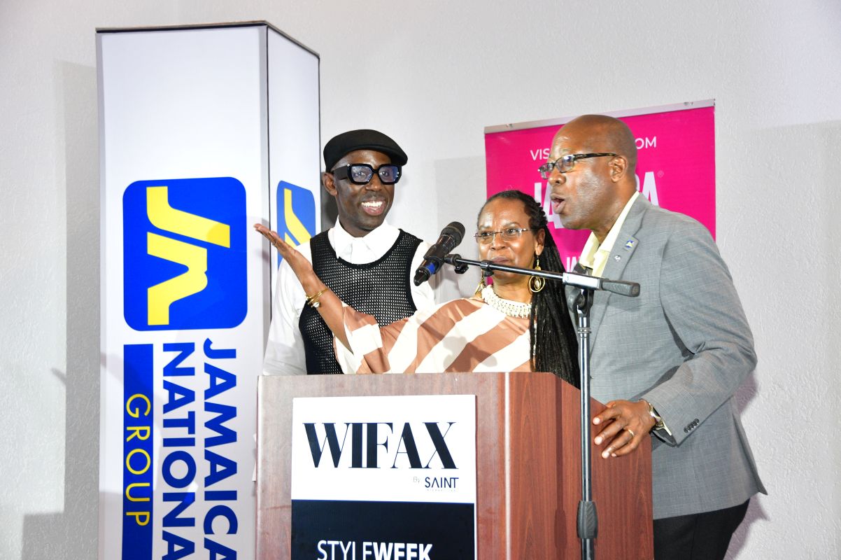 Three people at a podium speaking into microphones, with a Jamaica National Group banner beside them and a WIFAX sign on the lectern.