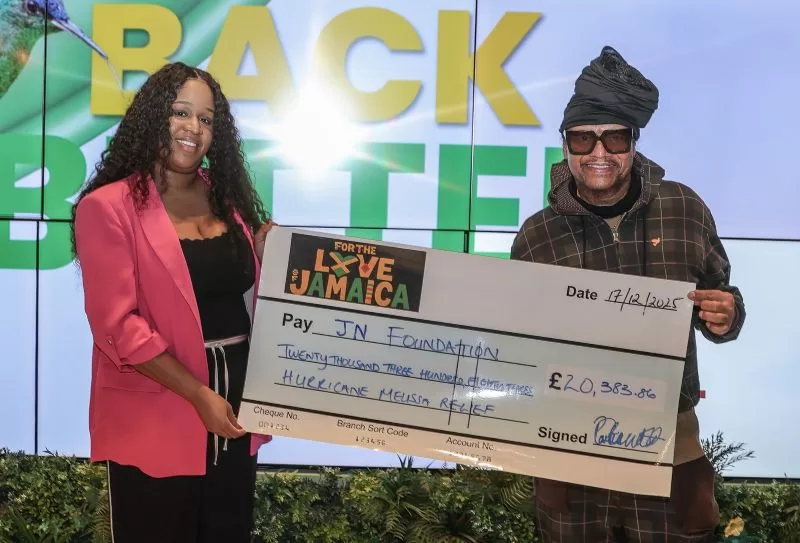 IMG_0238 - The Jamaica National Group Limited Two people smile on stage while presenting a large ceremonial cheque to the JN Foundation for hurricane relief, amount £20,383.86, with a colorful'For the Love Jamaica' logo on the cheque.