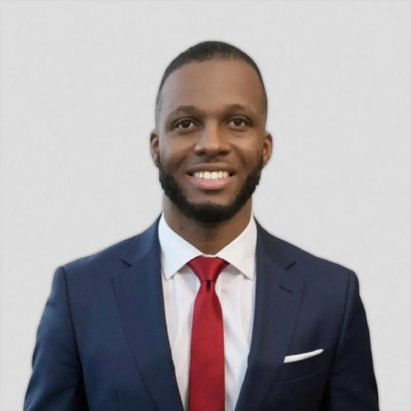 Professional portrait of a smiling man in a navy suit, white shirt, and red tie against a light background with a white pocket square.